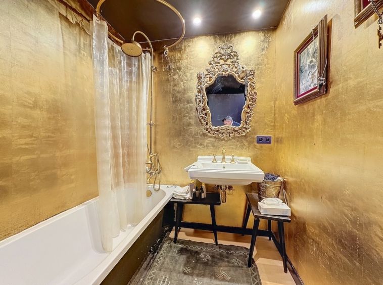 Salle de bain élégante avec murs en or, baignoire vintage, lavabo rétro et décor artistique raffinée.