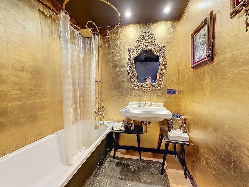 Salle de bain élégante avec murs en or, baignoire vintage, lavabo rétro et décor artistique raffinée.