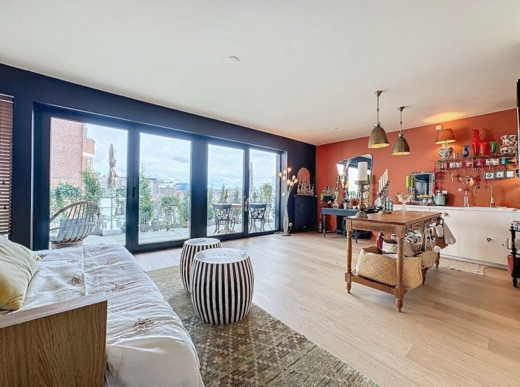 Salon moderne et chaleureux avec cuisine ouverte, grandes fenêtres, mobilier coloré et terrasse verdoyante.