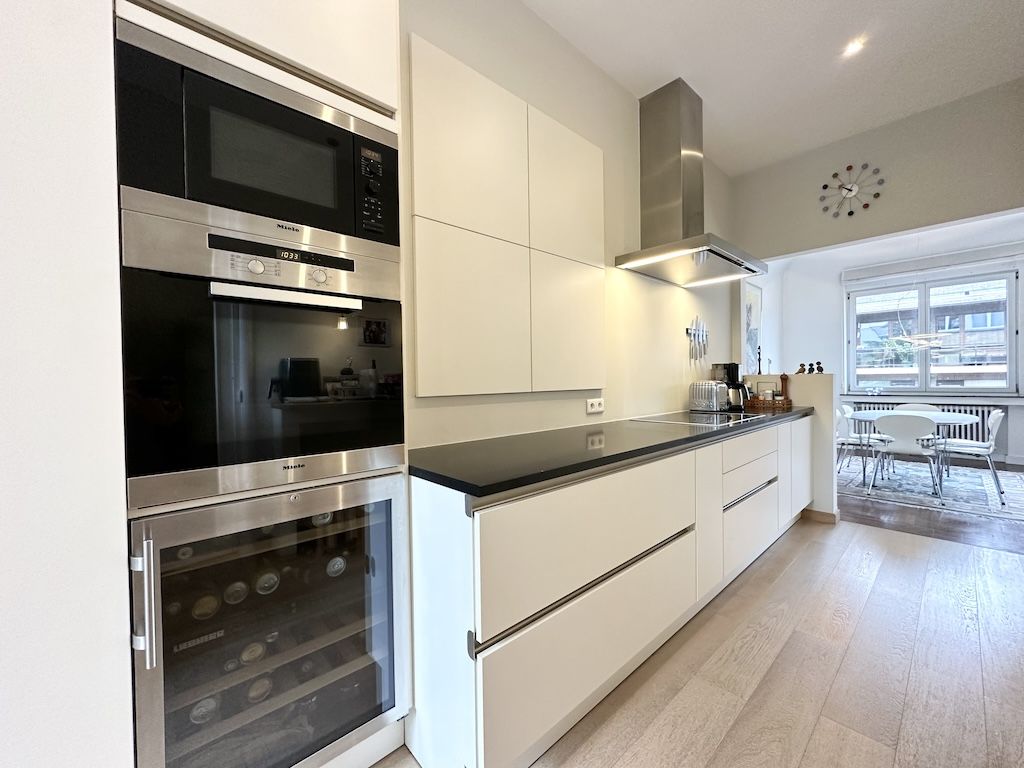 Cuisine moderne lumineuse avec meubles blancs, plans foncés, appareils en inox et espace convivial.