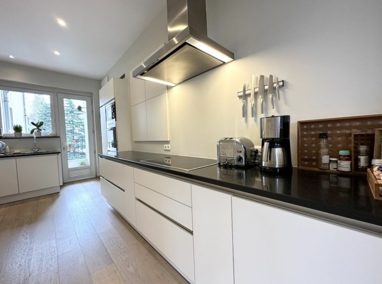 Cuisine moderne lumineuse avec plan de travail foncé, appareils intégrés, grande baie vitrée.