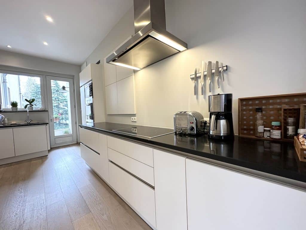 Cuisine moderne lumineuse avec plan de travail foncé, appareils intégrés, grande baie vitrée.