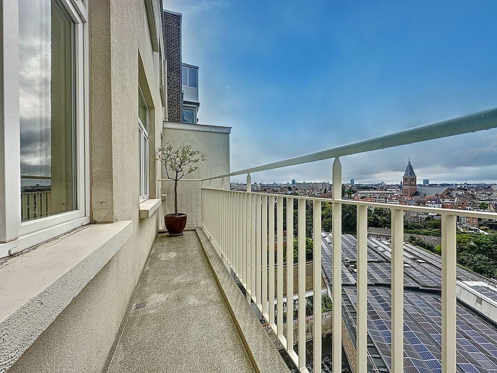 Balcon panoramique sur la ville, ciel bleu, buildings variés, végétation, ambiance apaisante.