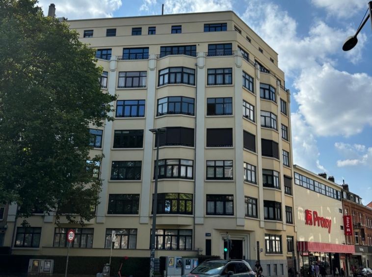 Bâtiment historique avec façades modernes, quartier vibrant, rues animées et ciel nuageux.