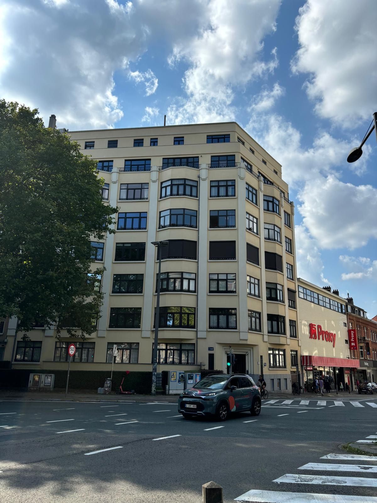 Bâtiment historique avec façades modernes, quartier vibrant, rues animées et ciel nuageux.