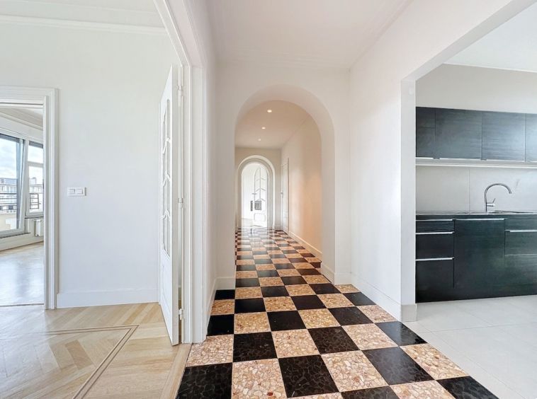 Couloir lumineux avec sol en carreaux checkérisés, arches arrondies et cuisine moderne noire.