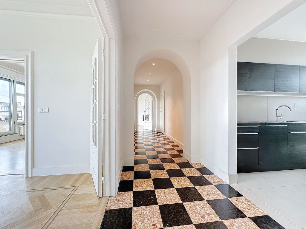 Couloir lumineux avec sol en carreaux checkérisés, arches arrondies et cuisine moderne noire.