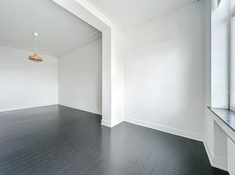 Espace minimaliste lumineux avec sols sombres, grande fenêtre, ambiance moderne et chaleureuse.