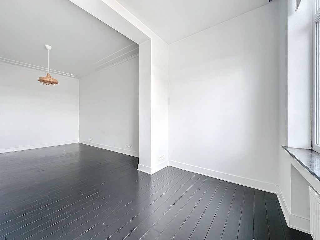 Espace minimaliste lumineux avec sols sombres, grande fenêtre, ambiance moderne et chaleureuse.