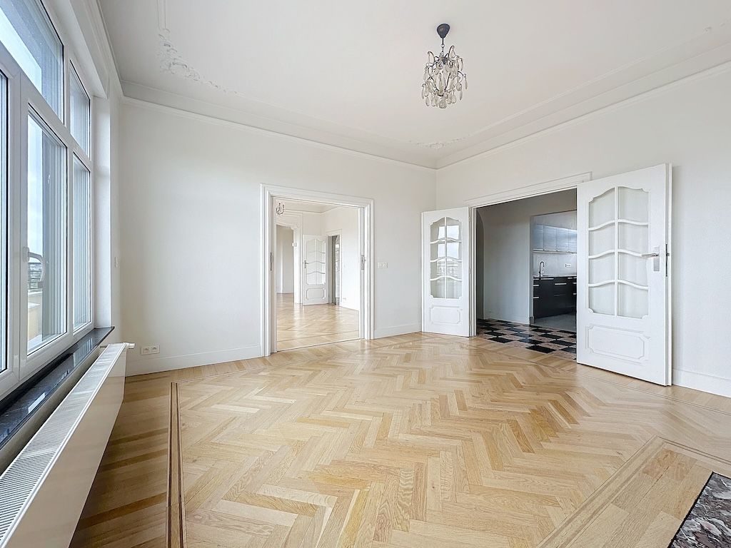 Salon lumineux avec parquet en chevron, grandes fenêtres, portes en verre et décoration moderne.