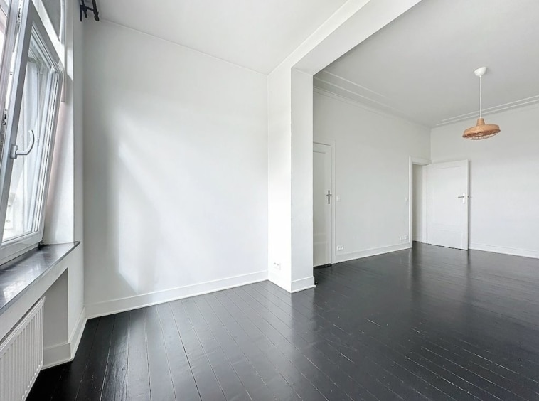 Intérieur moderne minimaliste avec murs blancs, sol en bois foncé, grande fenêtre et éclairage cuivre.