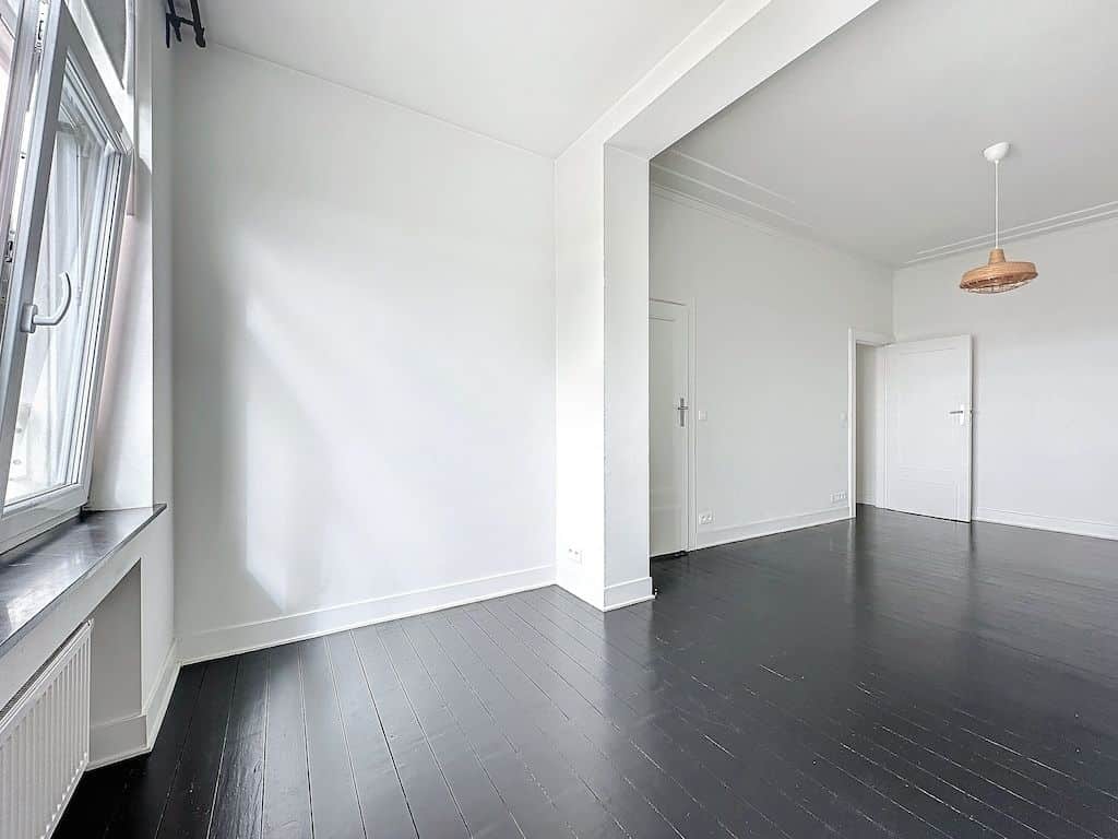Intérieur moderne minimaliste avec murs blancs, sol en bois foncé, grande fenêtre et éclairage cuivre.
