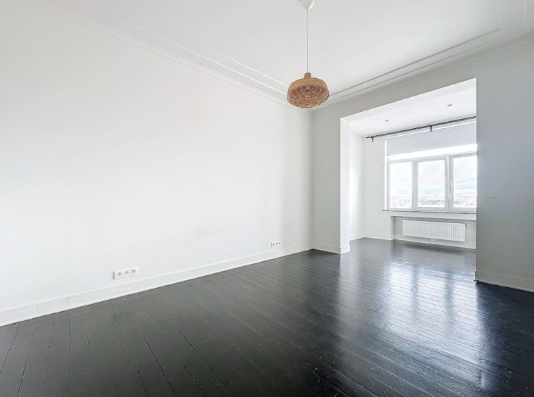 Espace moderne et lumineux avec murs blancs, sol en bois foncé et éclairage naturel ample.