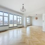 Salle lumineuse avec parquet chevron, large fenêtres, lustre élégant et moulures classiques.