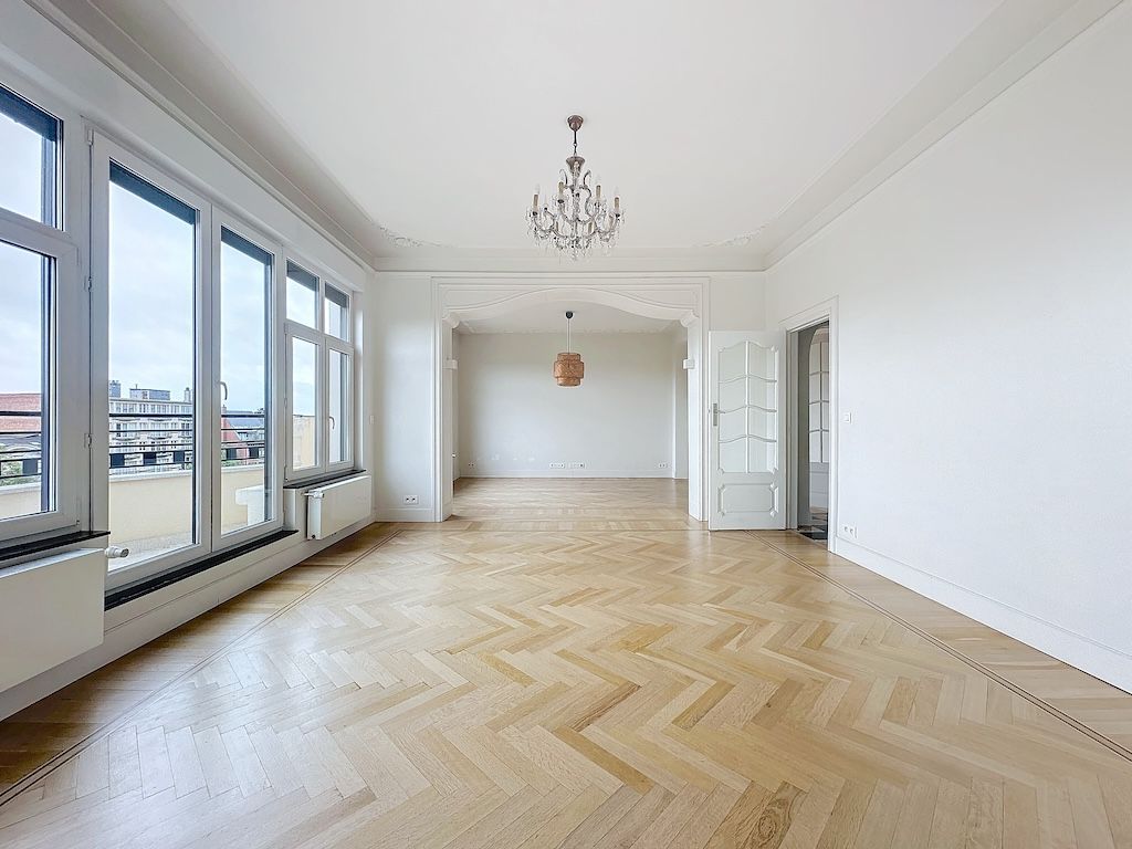 Salle lumineuse avec vue urbaine, parquet en chevrons, lustre élégant, espace minimaliste.