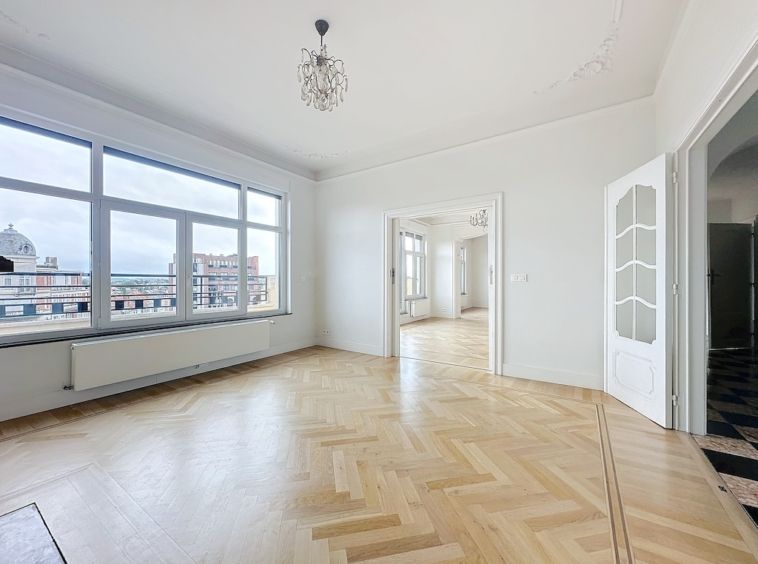 Salon panoramique lumineux avec parquet en chevrons, lustre élégant, ambiance moderne et chaleureuse.