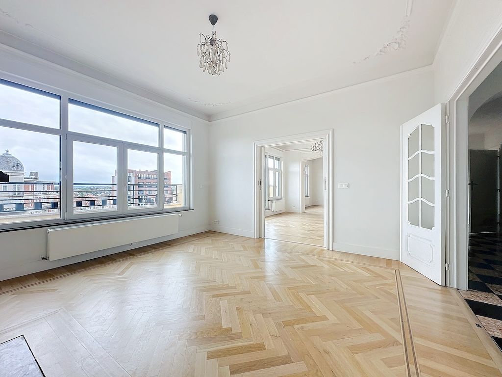Salon panoramique lumineux avec parquet en chevrons, lustre élégant, ambiance moderne et chaleureuse.