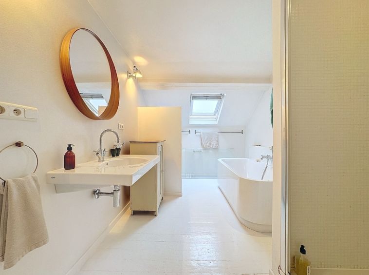 Salle de bain moderne blanche avec baignoire, lavabo double, miroir en bois et lumière naturelle.