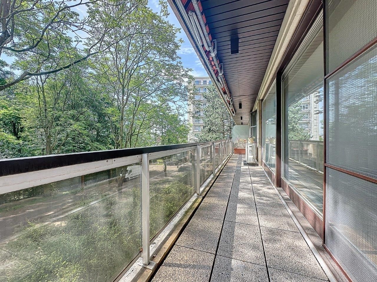 Balcon moderne en verre offrant une vue paisible sur la nature verdoyante sous un ciel ensoleillé.