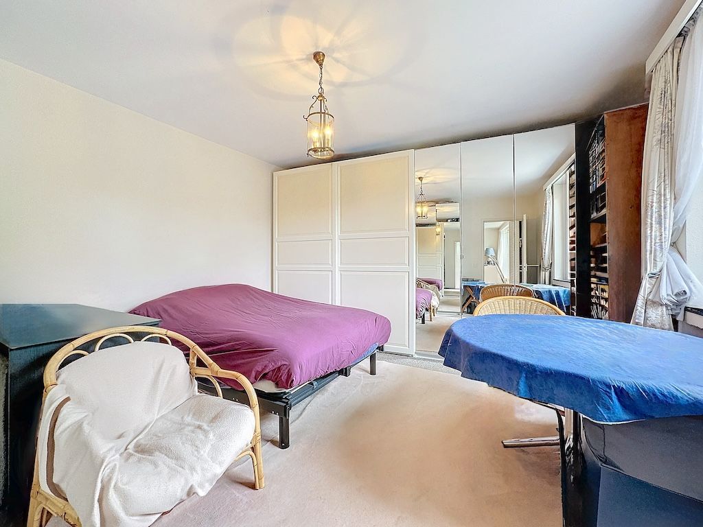 Chambre lumineuse avec deux lits, grand dressing miroir et fauteuil en rotin, ambiance chaleureuse.
