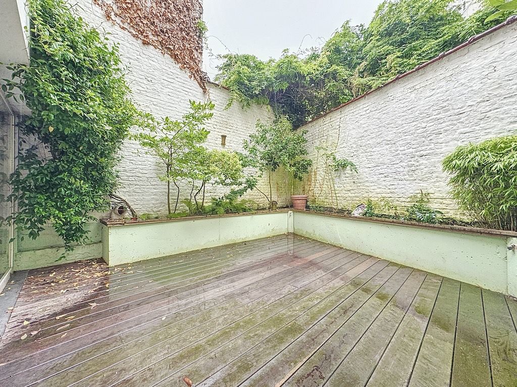 Cour de détente rustique avec murs blancs, végétation luxuriante et terrasse en bois humide.