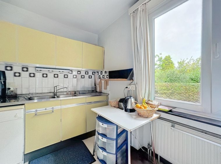 Cuisine lumineuse avec armoires jaunes, fenêtre naturelle, comptoir organisé, ambiance cosy et pratique.