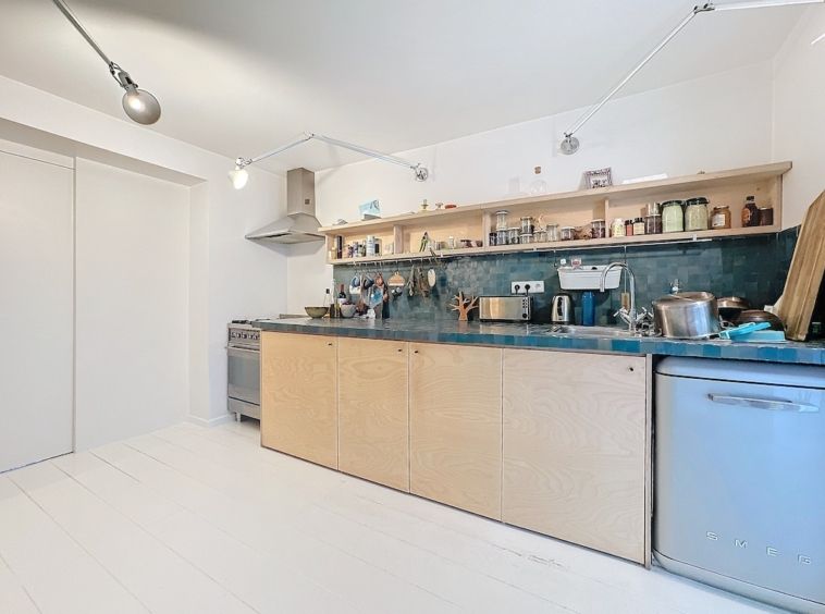 Cuisine moderne lumineuse, plan bleu, étagères en bois, appareils inox, décoration épurée.