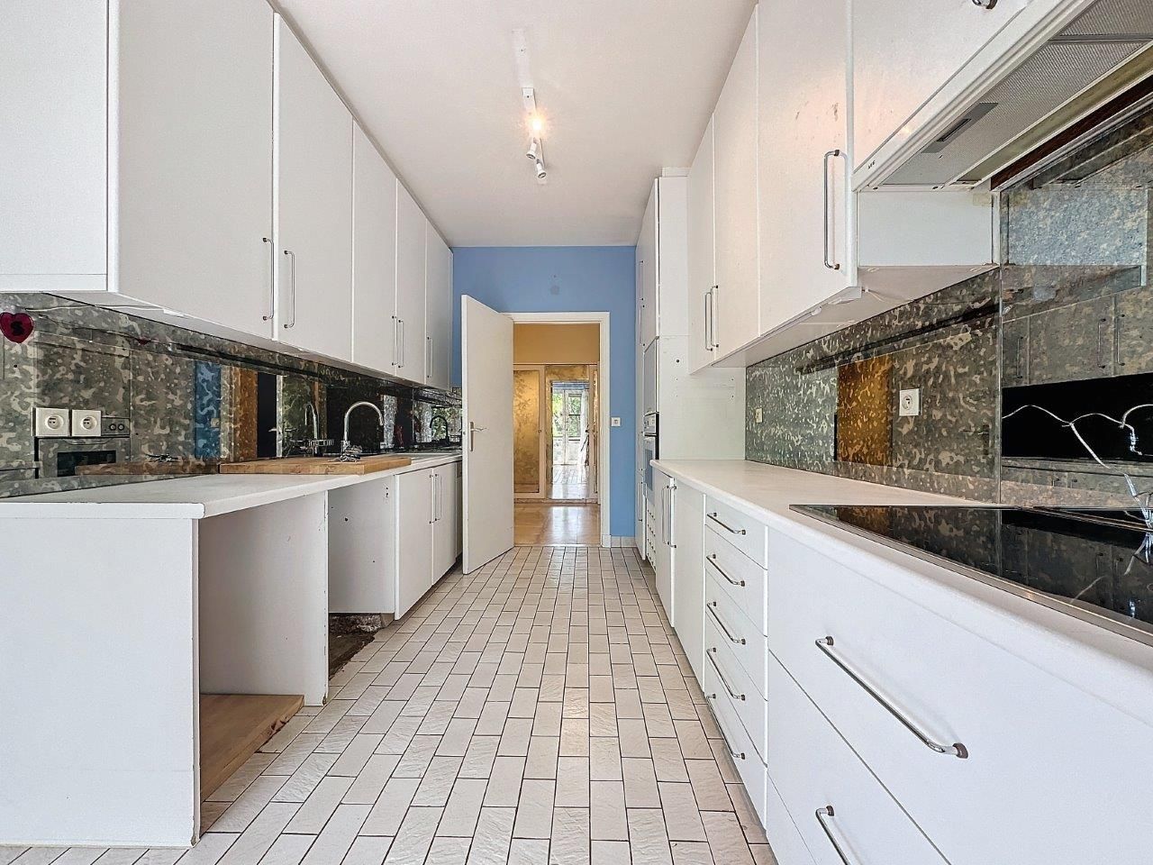 Cuisine contemporaine épurée avec meubles blancs, backsplash sombre et sol lumineux.