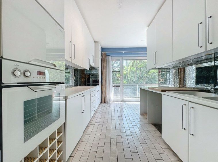 Cuisine moderne lumineuse avec meubles blancs, plan de travail clair, fenêtres spacieuses et carrelage en chevrons.