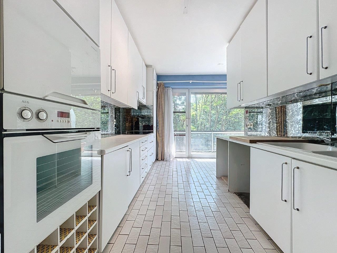 Cuisine moderne lumineuse avec meubles blancs, plan de travail clair, fenêtres spacieuses et carrelage en chevrons.