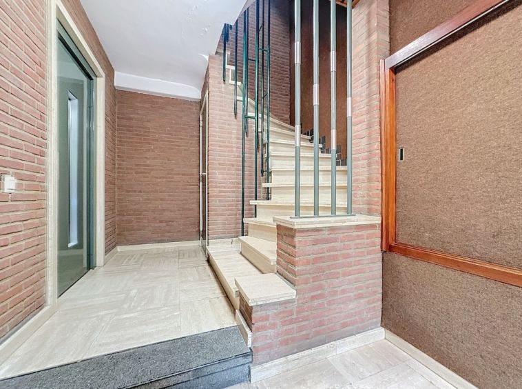Hall d’entrée moderne avec escalier en pierre, murs en brique chaleureuse et éclairage naturel.