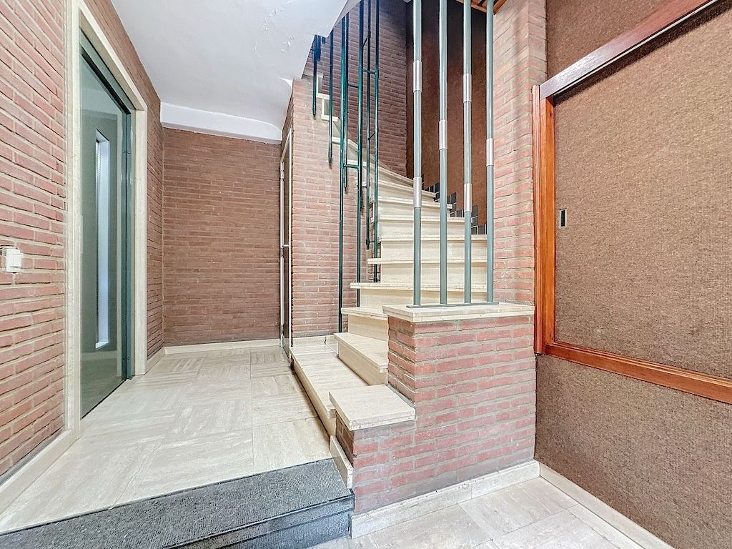 Hall d’entrée moderne avec escalier en pierre, murs en brique chaleureuse et éclairage naturel.