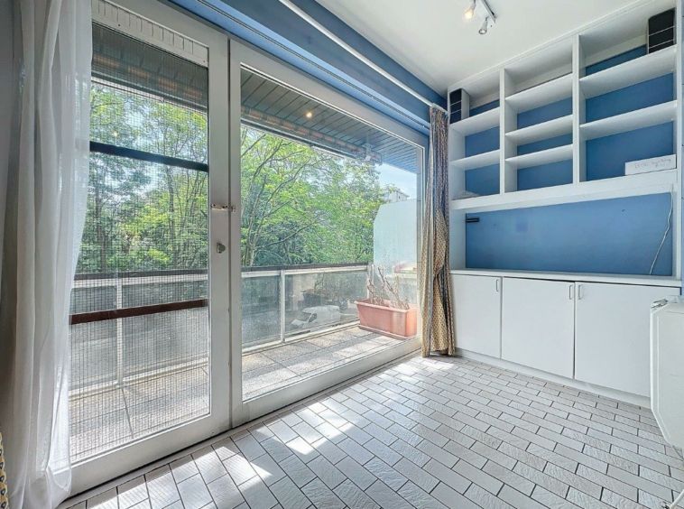 Intérieur moderne lumineux avec balcon verdoyant, étagères bleues et design épuré.