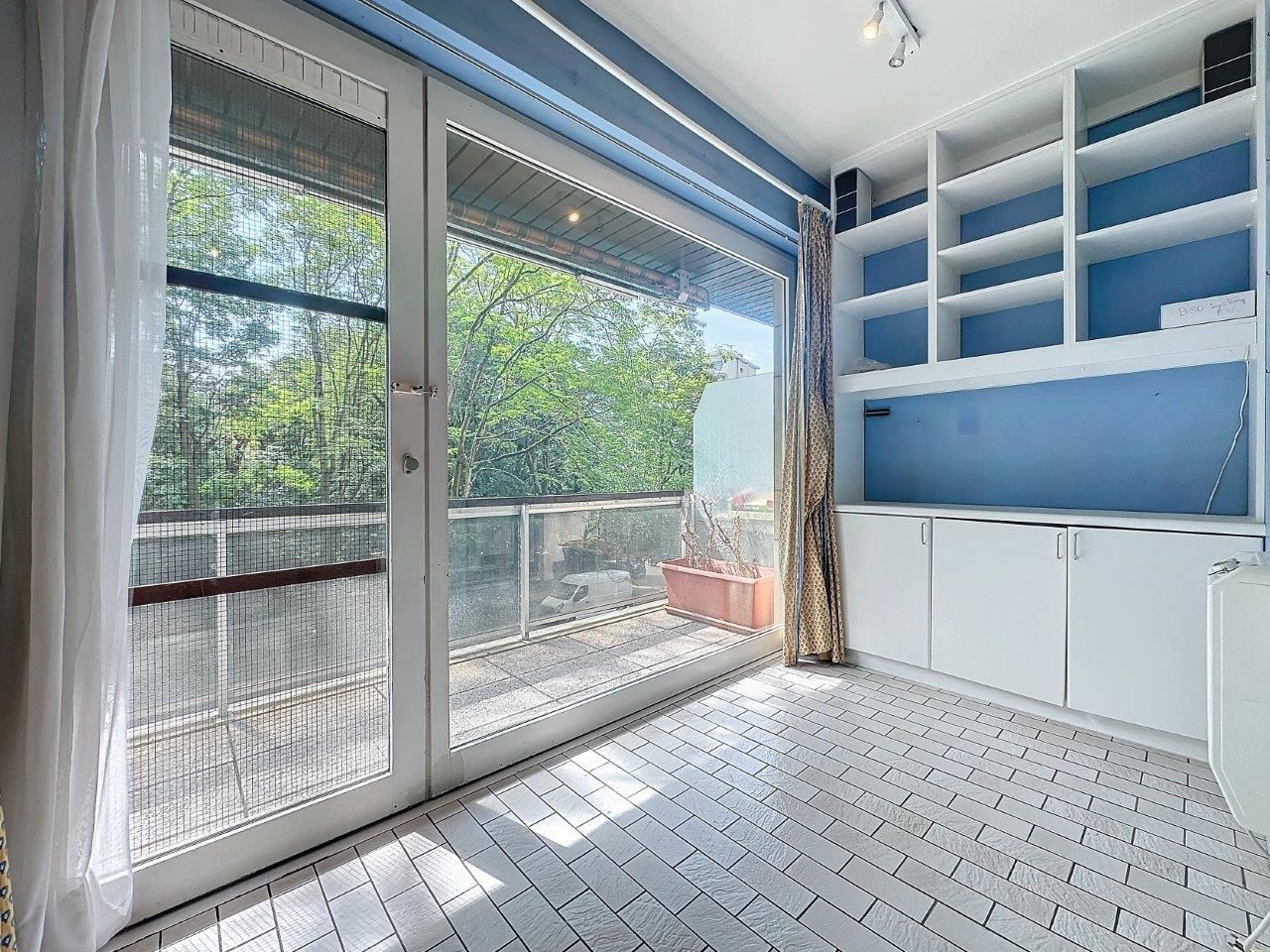 Intérieur moderne lumineux avec balcon verdoyant, étagères bleues et design épuré.
