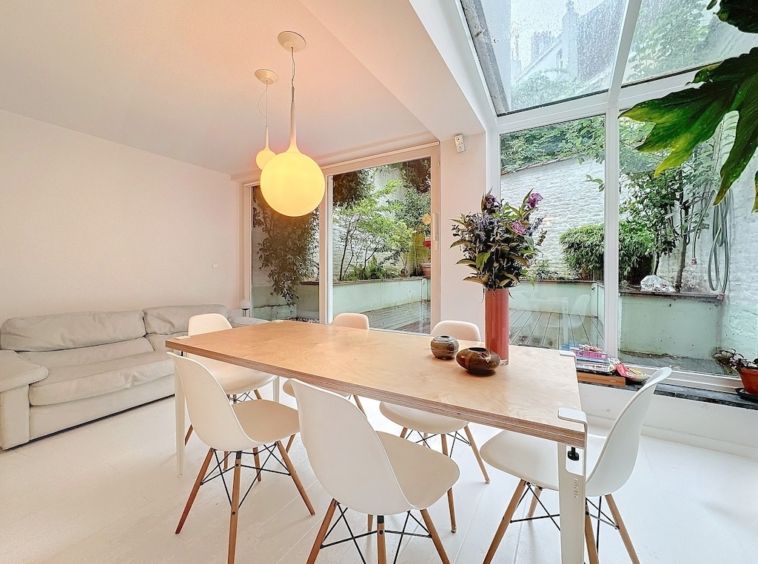 Salle à manger moderne lumineuse avec vue sur la nature, grande table en bois et décoration florale élégante.
