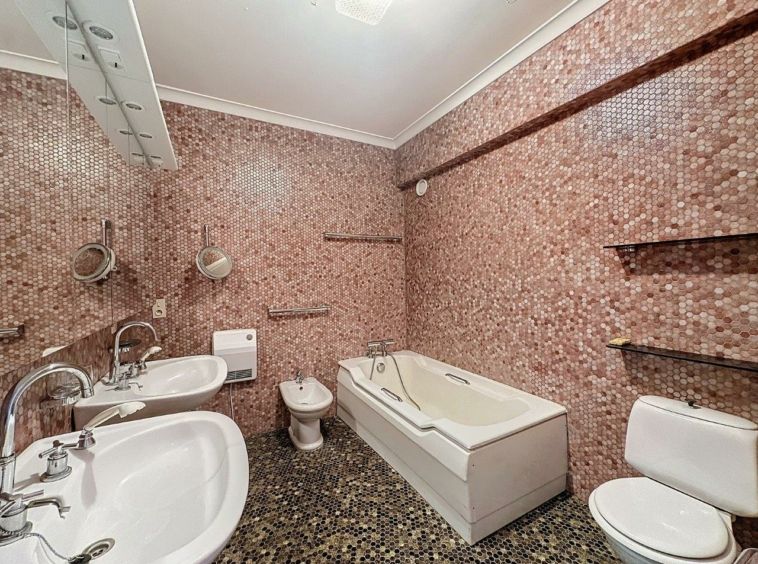 Salle de bain moderne avec murs rose, baignoire blanche, double lavabo et sol foncé en carreaux.