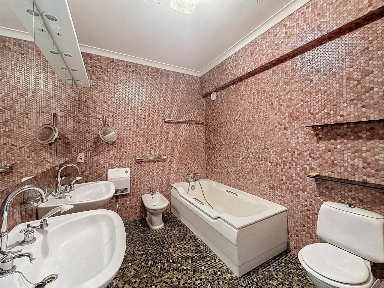 Salle de bain moderne avec murs rose, baignoire blanche, double lavabo et sol foncé en carreaux.