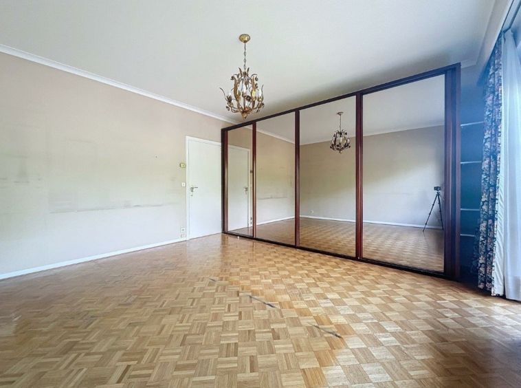 Salon chaleureux avec parquet, miroir, lustre classique et rideaux décoratifs élégants.