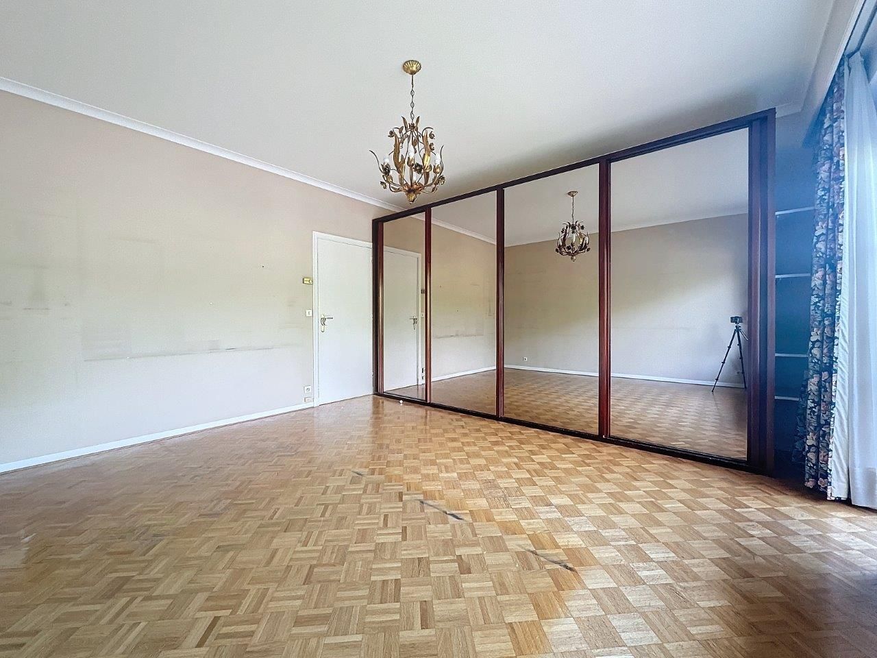 Salon chaleureux avec parquet, miroir, lustre classique et rideaux décoratifs élégants.