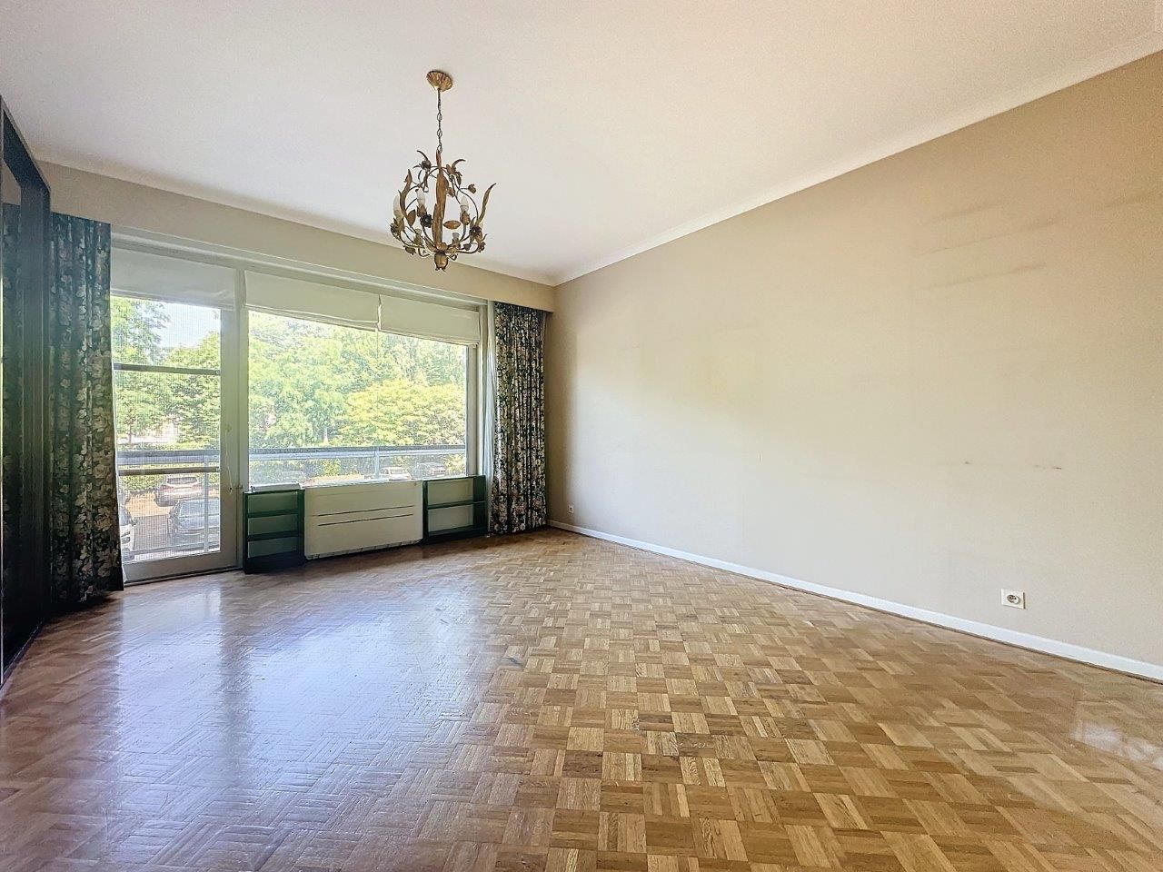 Salon lumineux minimaliste avec parquet, grande fenêtre, rideaux verts et éclairage vintage.