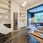 Salon moderne minimaliste avec mur bleu, meubles épurés, cheminée noire et lumière naturelle abondante.