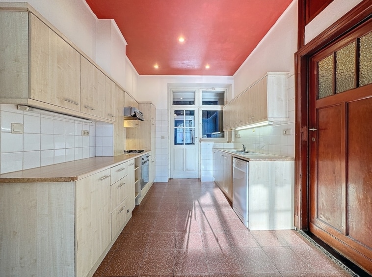 Cuisine moderne lumineuse avec éléments en bois clair, plafond rouge vif et grande fenêtre.