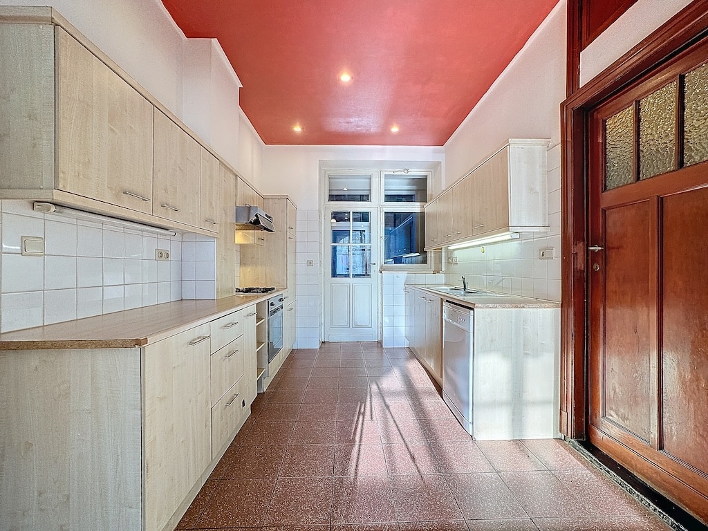 Cuisine moderne lumineuse avec éléments en bois clair, plafond rouge vif et grande fenêtre.