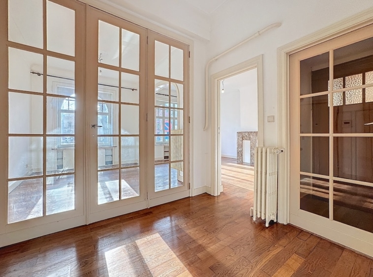 Intérieur lumineux avec parquet en bois, grandes fenêtres, portes en verre et ambiance élégante.