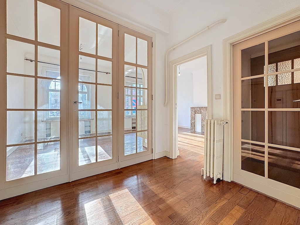 Intérieur lumineux avec parquet en bois, grandes fenêtres, portes en verre et ambiance élégante.