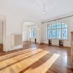 Intérieur lumineux et minimaliste avec hauts plafonds, grandes fenêtres, sol en bois et colonne en pierre.