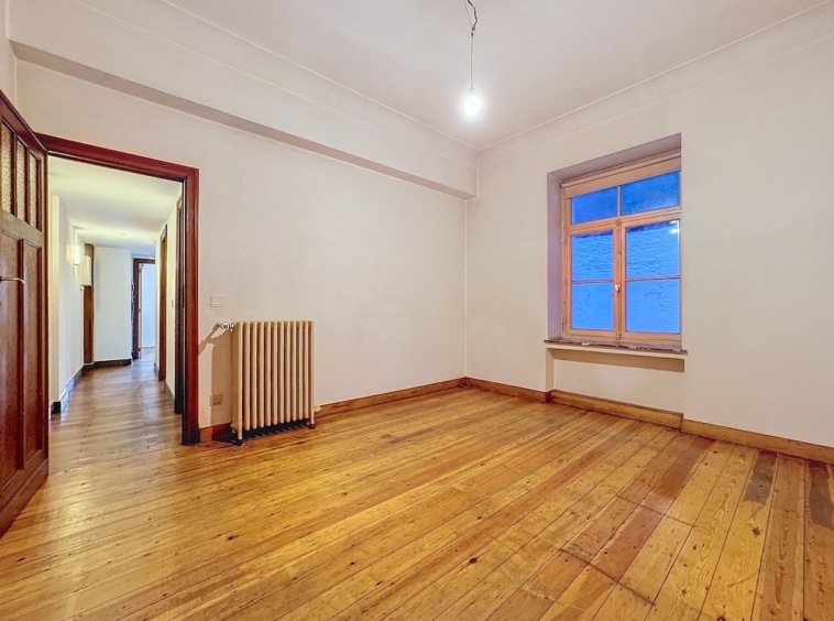 Espace lumineux et minimaliste avec sol en bois, grande fenêtre et ambiance chaleureuse adaptable.