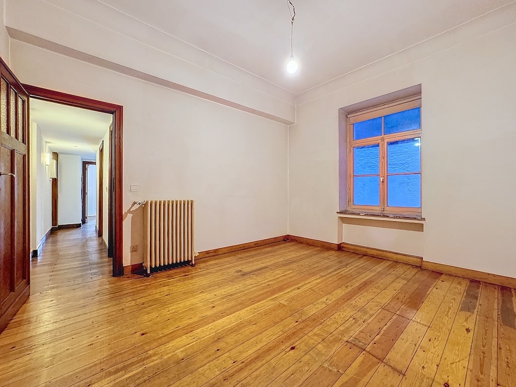Espace lumineux et minimaliste avec sol en bois, grande fenêtre et ambiance chaleureuse adaptable.