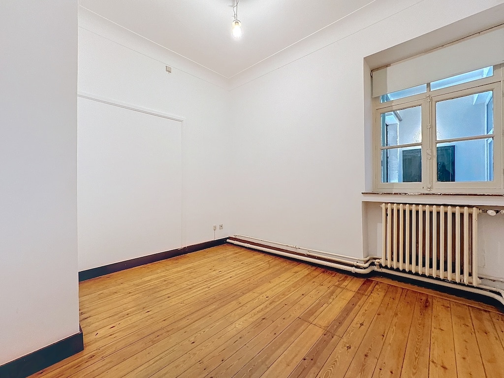 Espace moderne lumineux avec murs blancs, parquet en bois, fenêtre à volets et radiateur intégré.