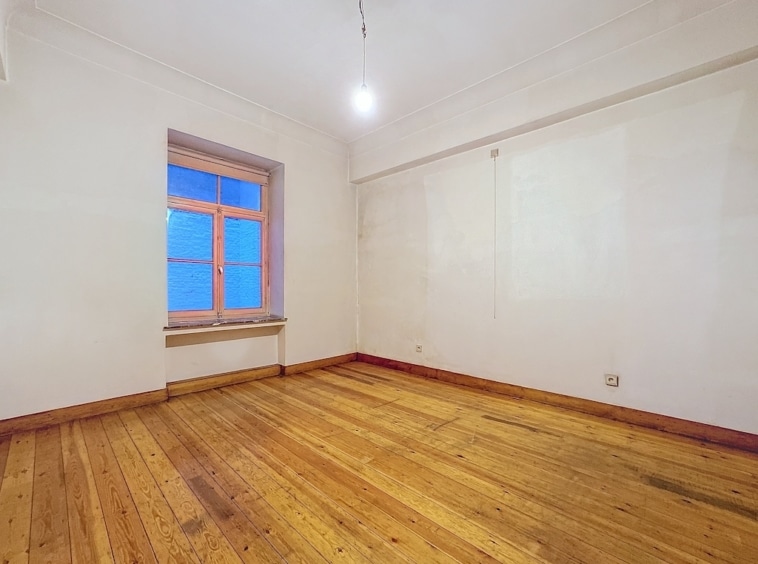 Salle lumineuse et minimaliste avec fenêtres, sol en bois naturel, ambiance chaleureuse et versatile.